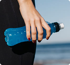 Persona sosteniendo una botella de bebida azul en un entorno exterior